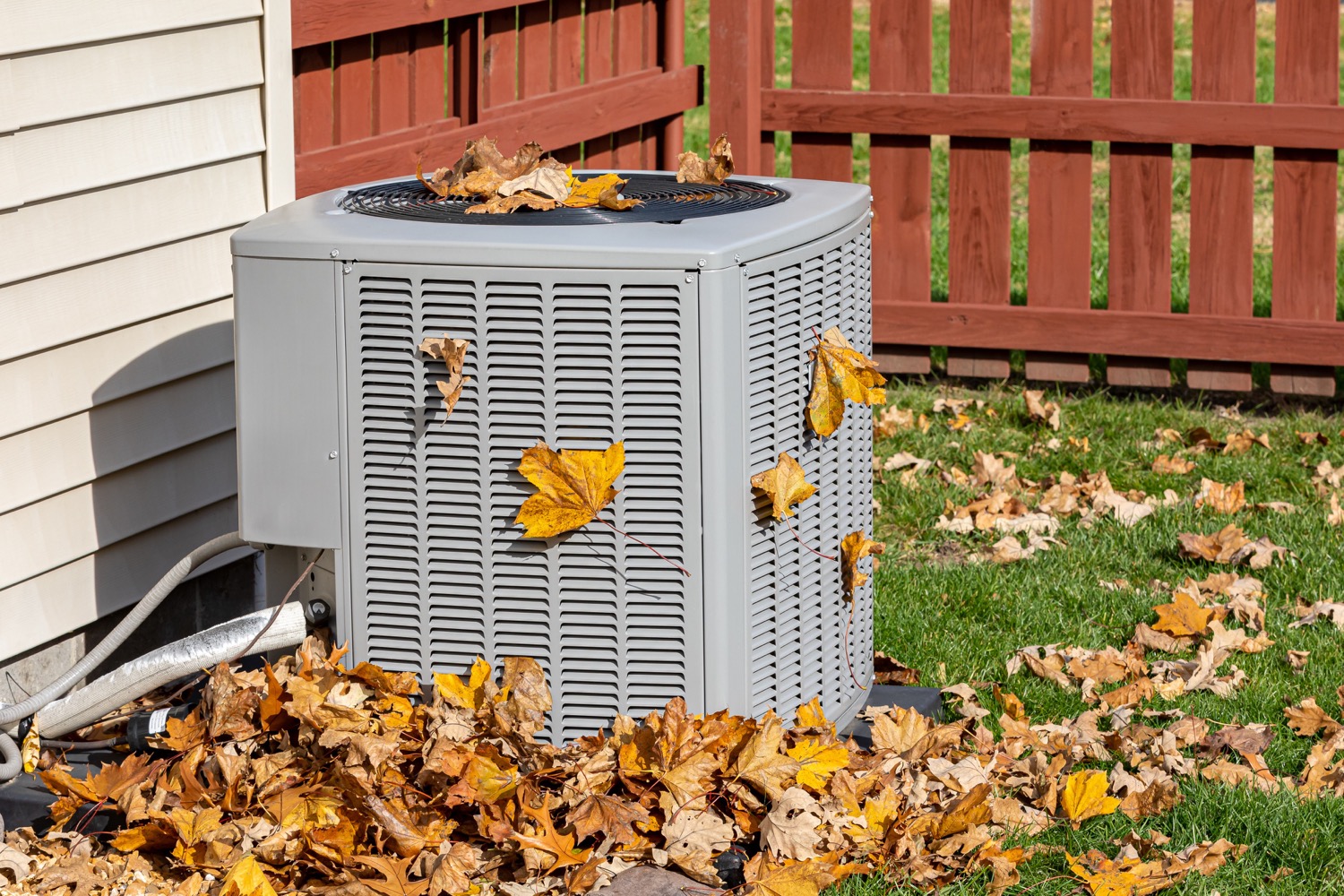 Leaves scattered on and around an outdoor HVAC unit highlighting the importance of seasonal maintenance